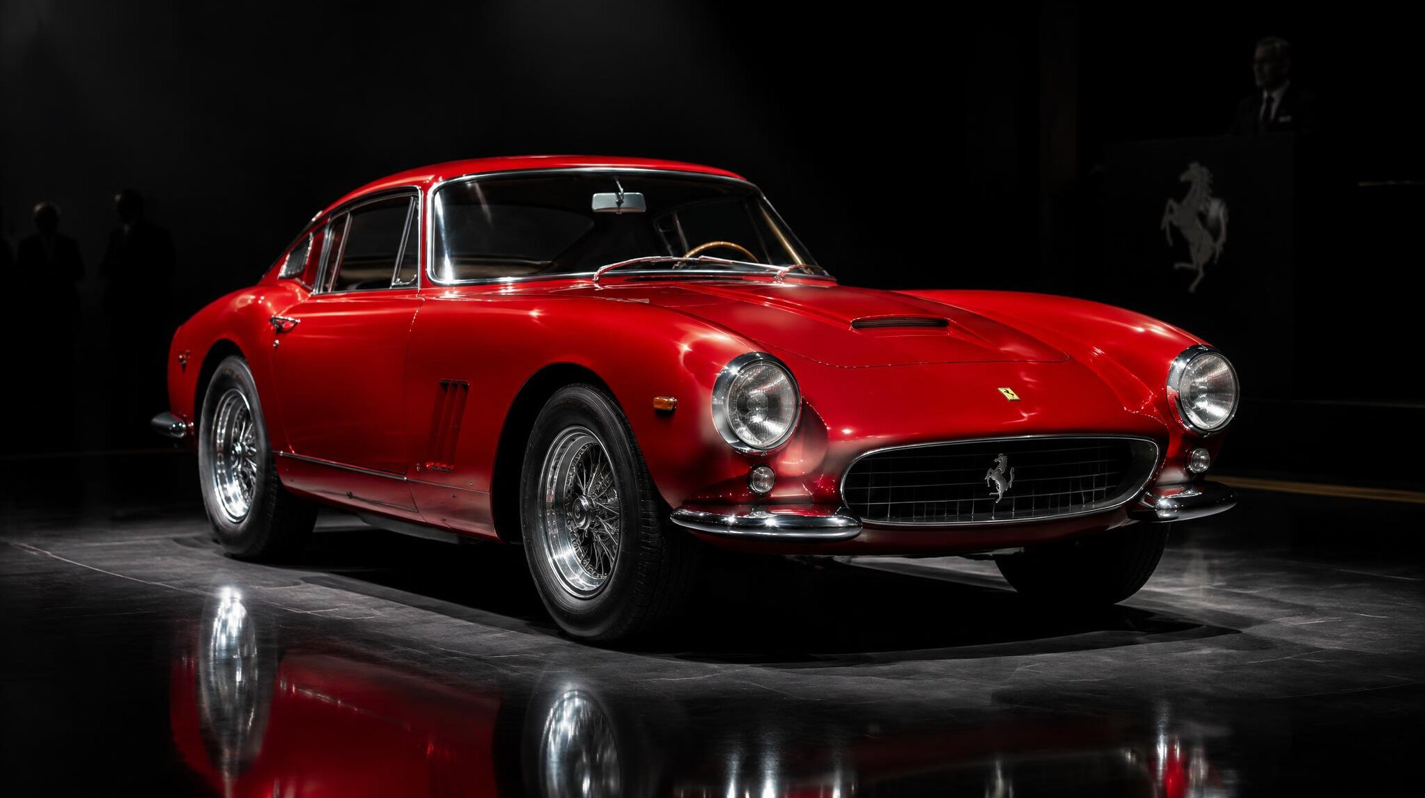 Red vintage Italian sports car under spotlight at a private auction event
